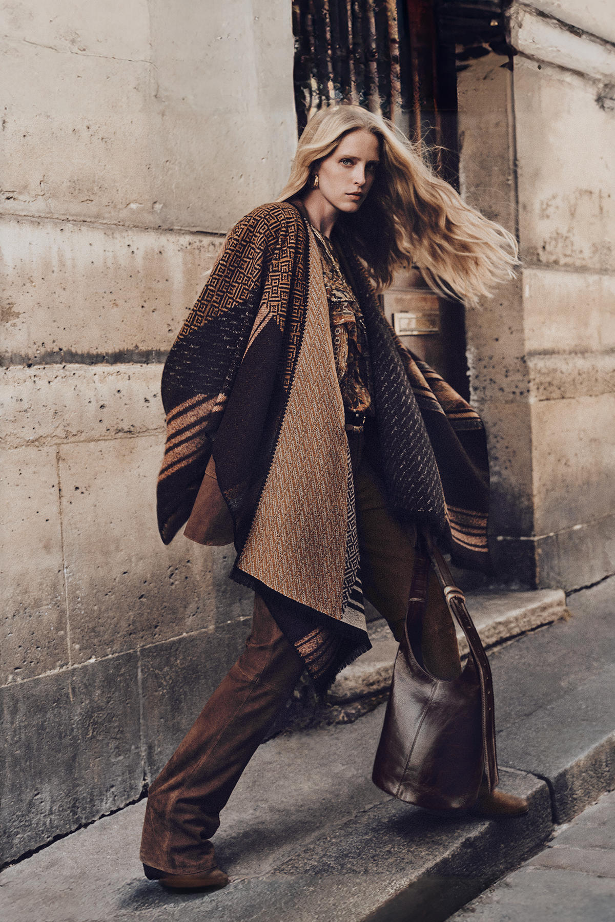 Blond hair model wearing a patern poncho with pants and the new iconic YouYou bag